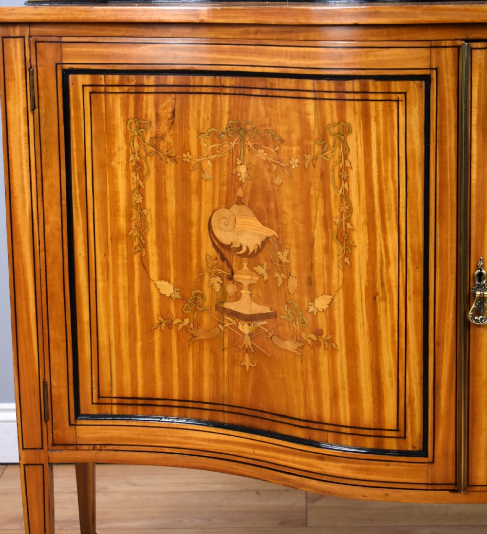 A 19th-century satinwood display cabinet featuring a serpentine glazed upper section and inlaid lower cupboard doors. View V