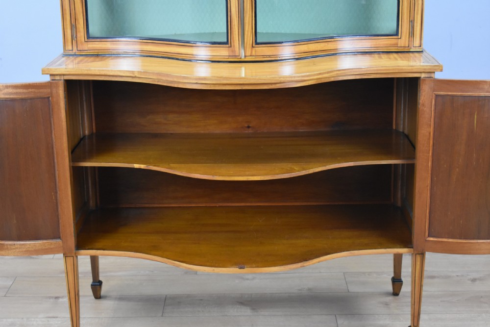 A 19th-century satinwood display cabinet featuring a serpentine glazed upper section and inlaid lower cupboard doors. View IX