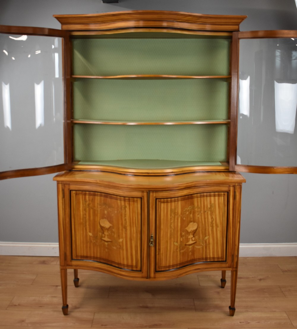 A 19th-century satinwood display cabinet featuring a serpentine glazed upper section and inlaid lower cupboard doors. View X