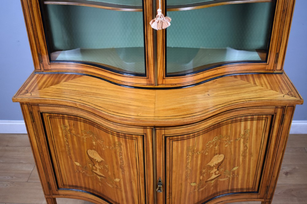 A 19th-century satinwood display cabinet featuring a serpentine glazed upper section and inlaid lower cupboard doors. View XII