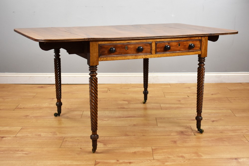 A Regency period mahogany drop-leaf table featuring two drawers with dark turned knobs and four spiral-carved legs on brass castors. View II