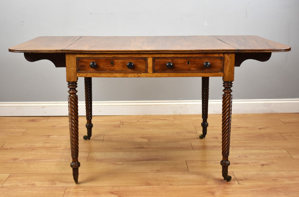A Regency period mahogany drop-leaf table featuring two drawers with dark turned knobs and four spiral-carved legs on brass castors. View III