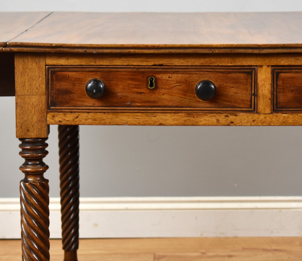 A Regency period mahogany drop-leaf table featuring two drawers with dark turned knobs and four spiral-carved legs on brass castors. View IV