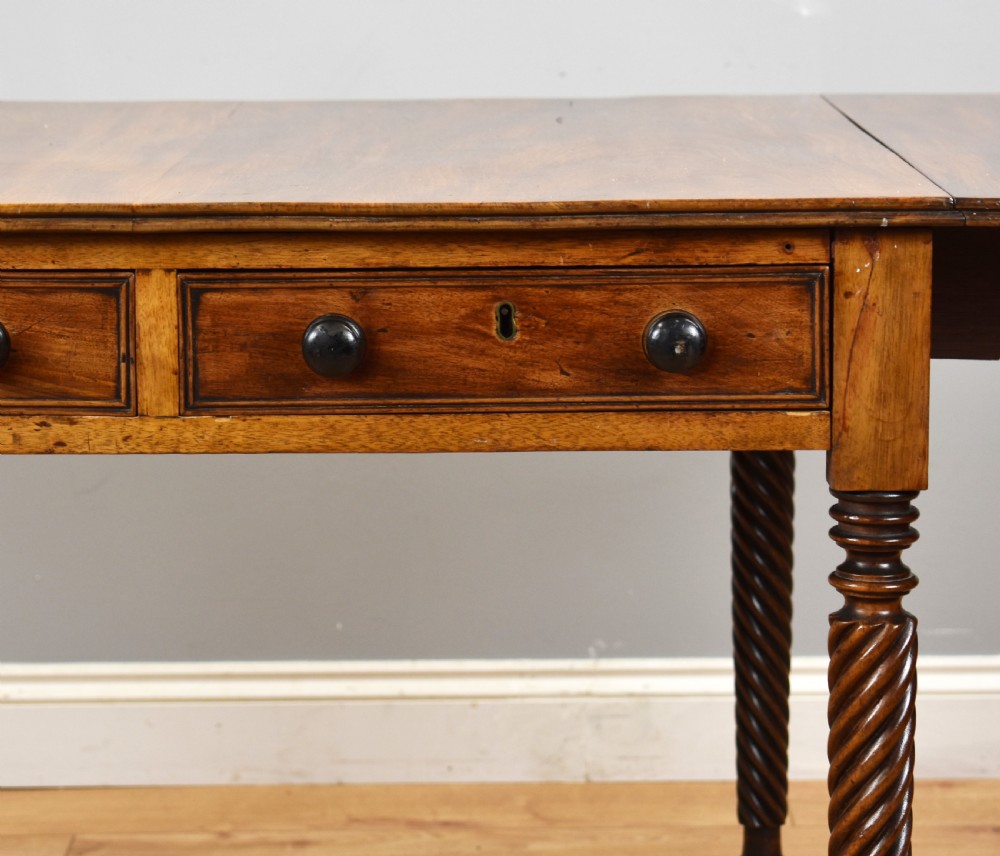 A Regency period mahogany drop-leaf table featuring two drawers with dark turned knobs and four spiral-carved legs on brass castors. View V