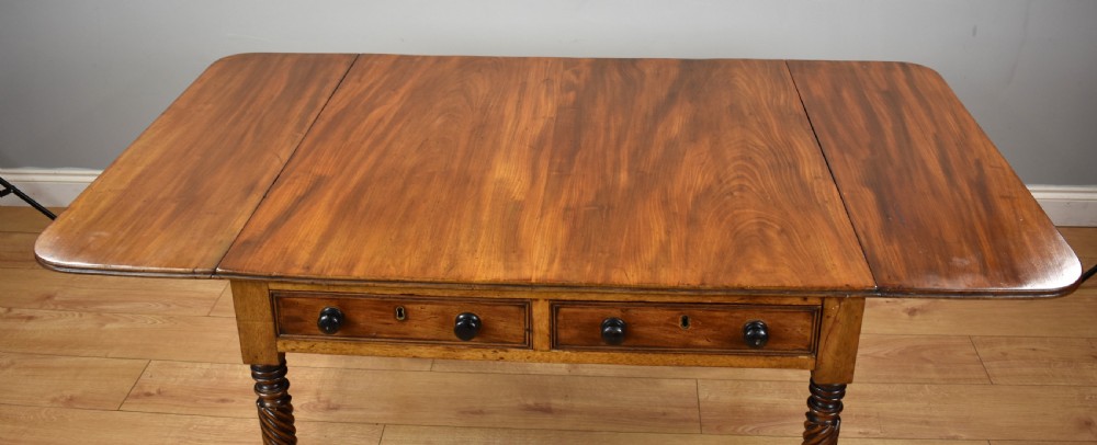 A Regency period mahogany drop-leaf table featuring two drawers with dark turned knobs and four spiral-carved legs on brass castors. View VII
