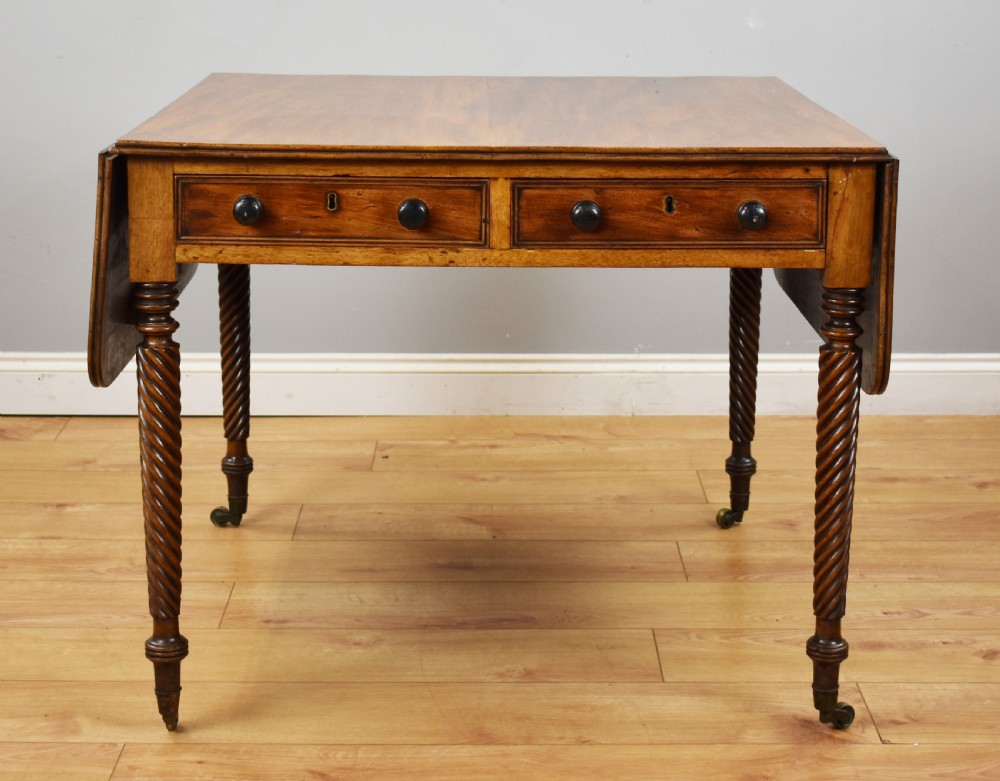 A Regency period mahogany drop-leaf table featuring two drawers with dark turned knobs and four spiral-carved legs on brass castors. View VIII