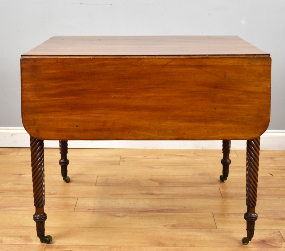 A Regency period mahogany drop-leaf table featuring two drawers with dark turned knobs and four spiral-carved legs on brass castors. View IX