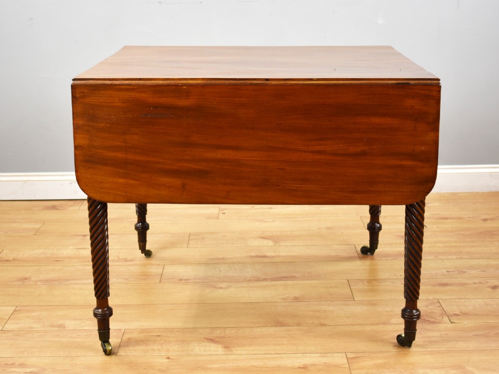 A Regency period mahogany drop-leaf table featuring two drawers with dark turned knobs and four spiral-carved legs on brass castors. View X