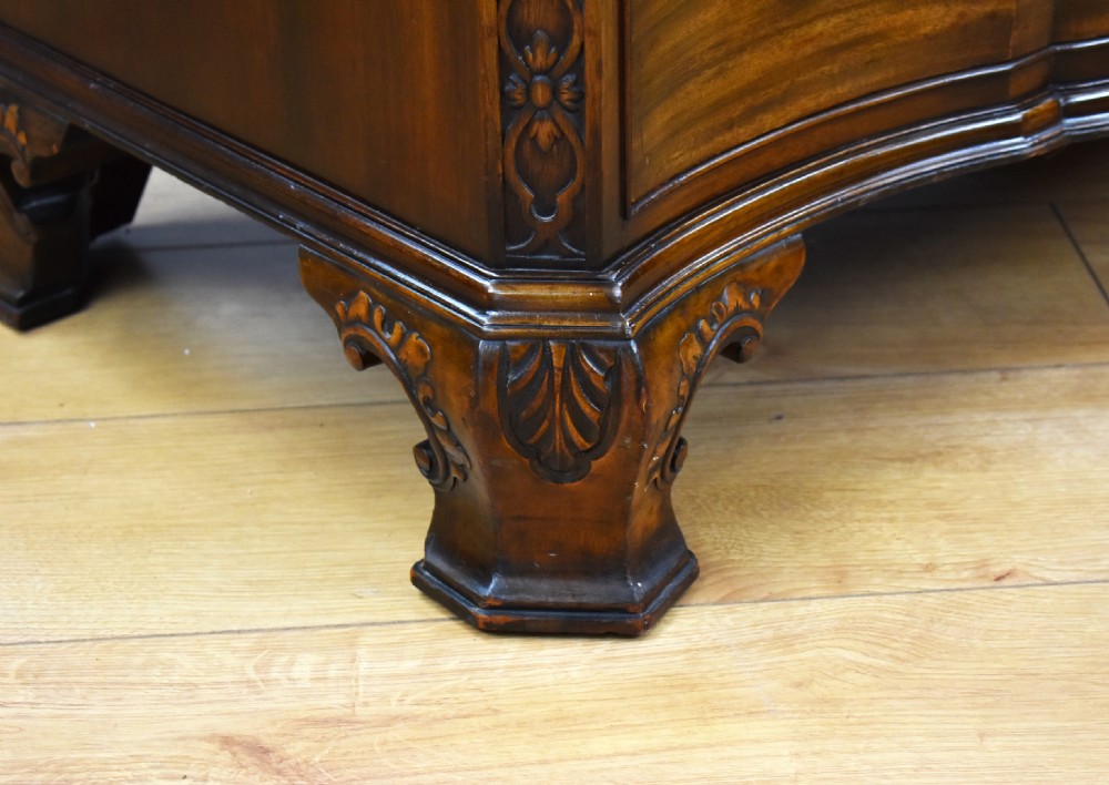 A dark mahogany serpentine-front chest of four drawers with brass handles, carved canted corners, and bracket feet. View IV