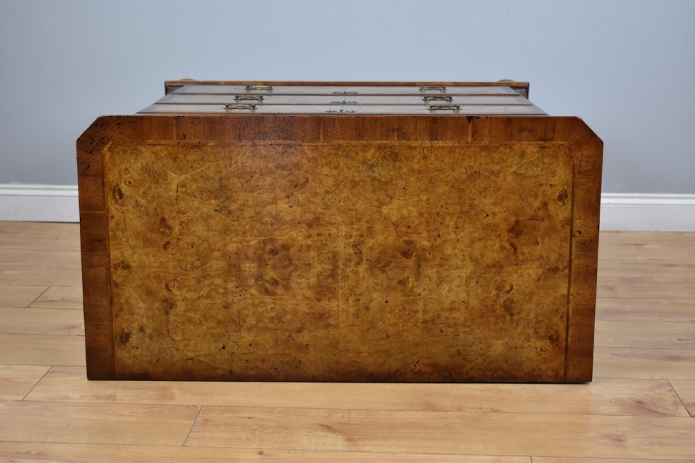 A George III burr walnut chest of drawers featuring two short drawers over three long drawers with crossbanded borders, brass escutcheons, and bun feet. View V