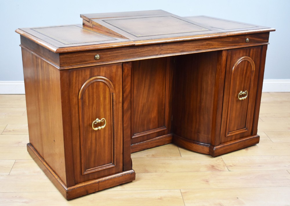 A Victorian mahogany kneehole desk with three leather-inlaid writing panels, twin pedestals featuring arched mouldings, and brass handles.