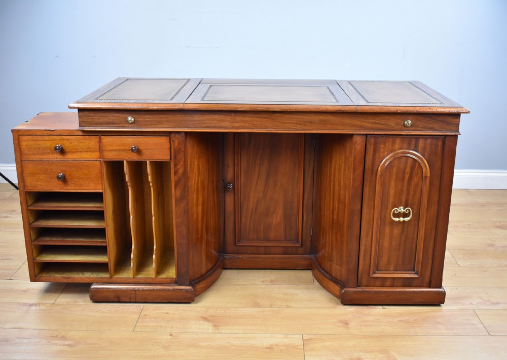 A Victorian mahogany kneehole desk with three leather-inlaid writing panels, twin pedestals featuring arched mouldings, and brass handles. View V