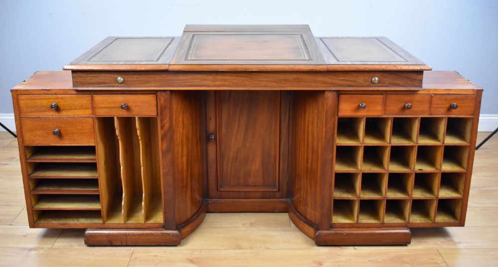 A Victorian mahogany kneehole desk with three leather-inlaid writing panels, twin pedestals featuring arched mouldings, and brass handles. View VI