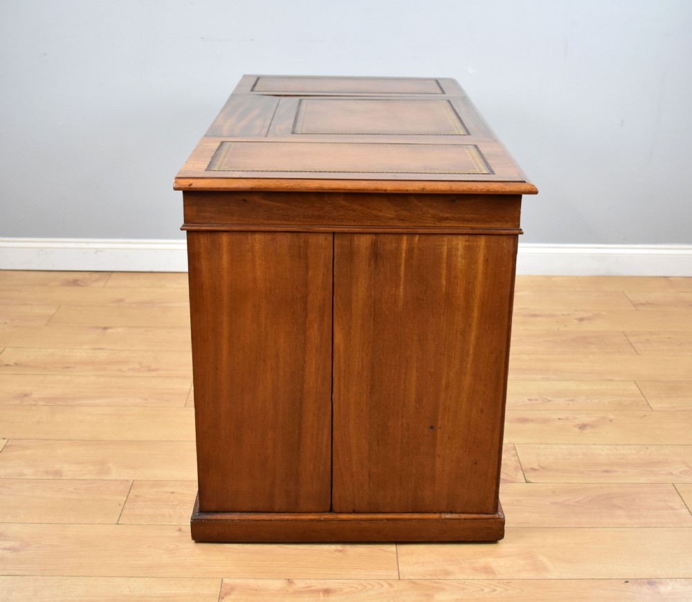 A Victorian mahogany kneehole desk with three leather-inlaid writing panels, twin pedestals featuring arched mouldings, and brass handles. View VIII