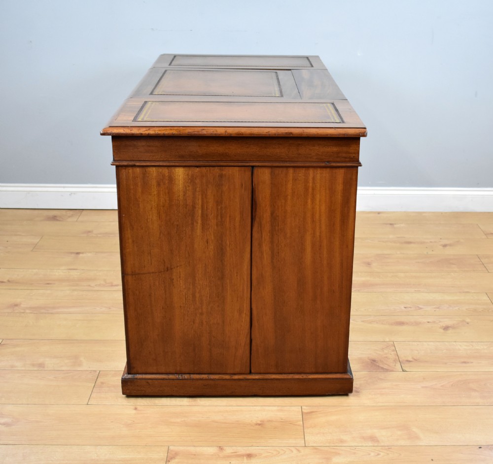 A Victorian mahogany kneehole desk with three leather-inlaid writing panels, twin pedestals featuring arched mouldings, and brass handles. View X