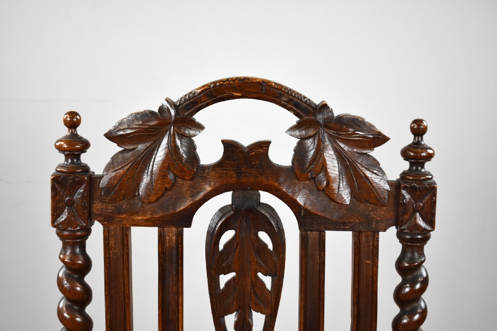A pair of dark oak armchairs featuring barley twist uprights, high backs with leaf carvings, and red leather upholstered seats. View XVIII