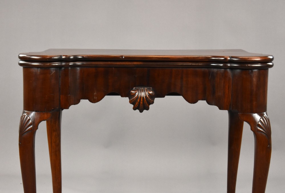 An 18th-century George II Irish mahogany fold-over card table with carved shell knees, a scalloped apron, and slender cabriole legs. View V