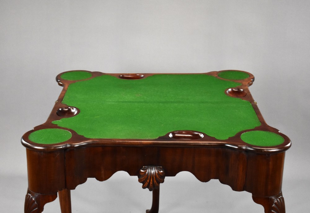 An 18th-century George II Irish mahogany fold-over card table with carved shell knees, a scalloped apron, and slender cabriole legs. View X