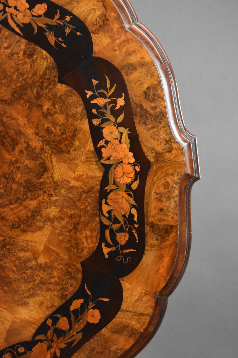 A Victorian burr walnut tilt-top breakfast table featuring a scalloped edge, intricate floral marquetry inlay border, and a carved four-star pedestal base. View V