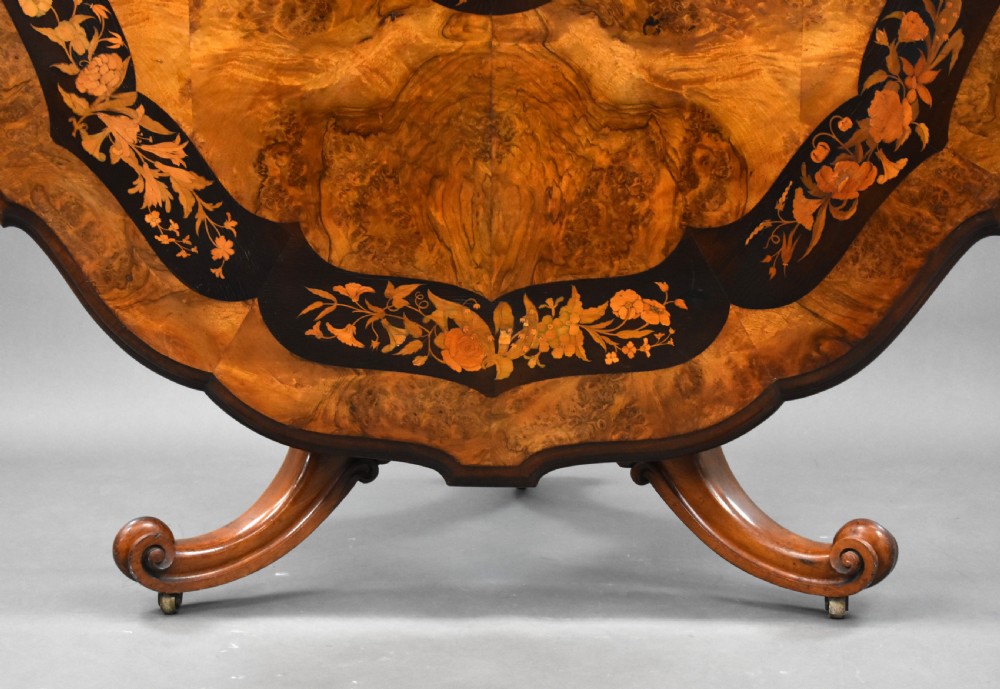 A Victorian burr walnut tilt-top breakfast table featuring a scalloped edge, intricate floral marquetry inlay border, and a carved four-star pedestal base. View VI
