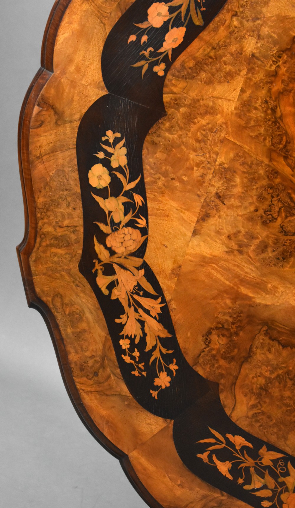 A Victorian burr walnut tilt-top breakfast table featuring a scalloped edge, intricate floral marquetry inlay border, and a carved four-star pedestal base. View VII