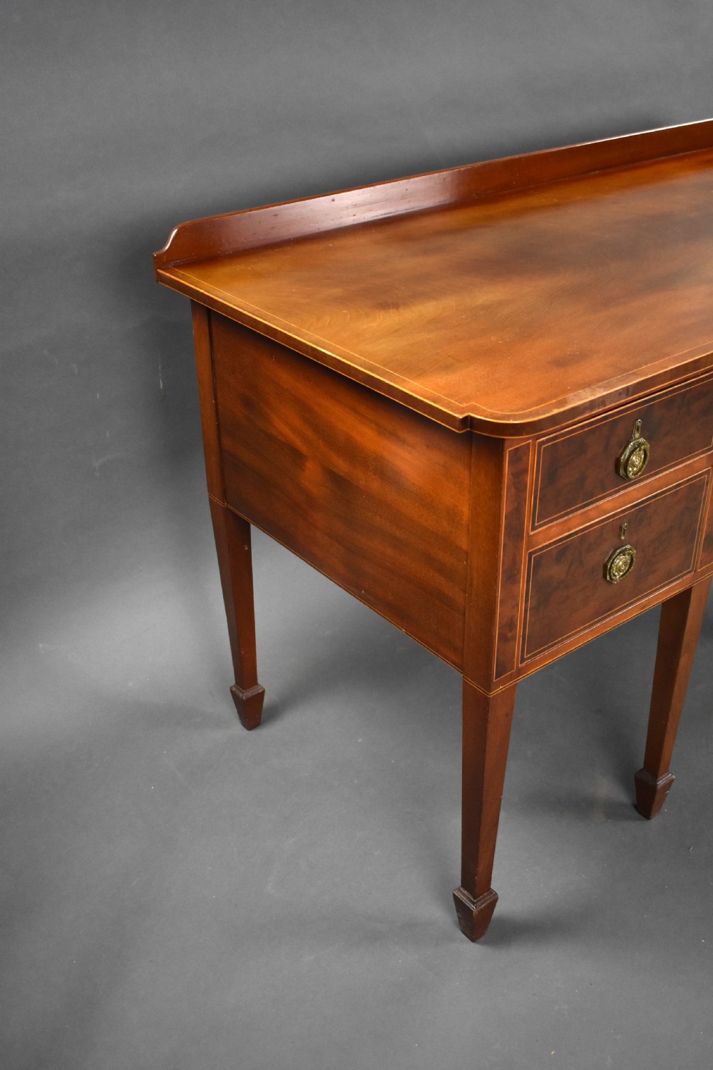 A nineteenth-century mahogany sideboard featuring a central kneehole arch, five inlaid drawers with brass rosette pull handles, and square tapered legs terminating in spade feet. View V