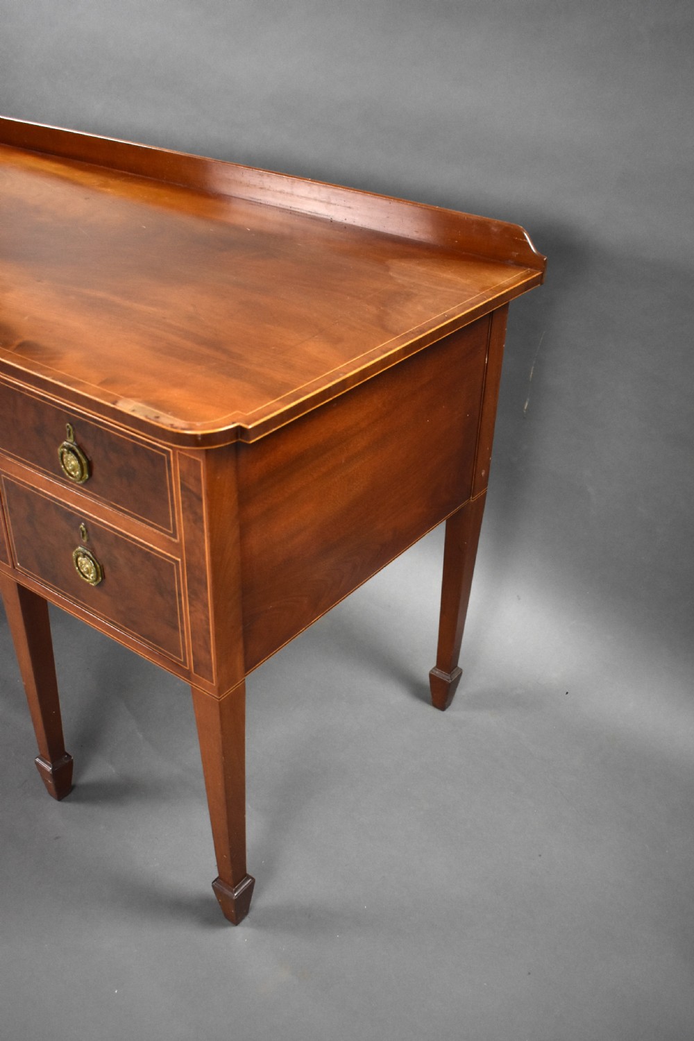 A nineteenth-century mahogany sideboard featuring a central kneehole arch, five inlaid drawers with brass rosette pull handles, and square tapered legs terminating in spade feet. View VI
