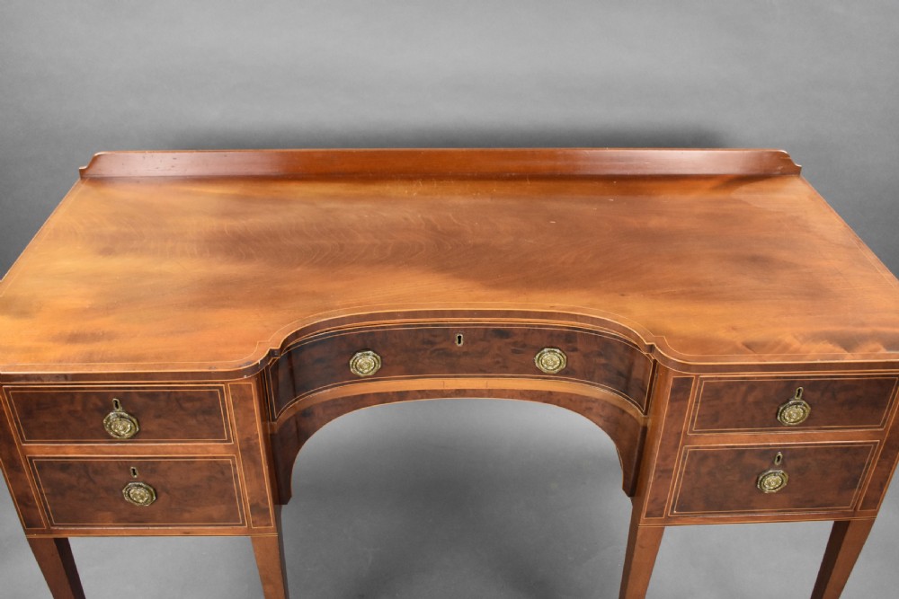 A nineteenth-century mahogany sideboard featuring a central kneehole arch, five inlaid drawers with brass rosette pull handles, and square tapered legs terminating in spade feet. View VII