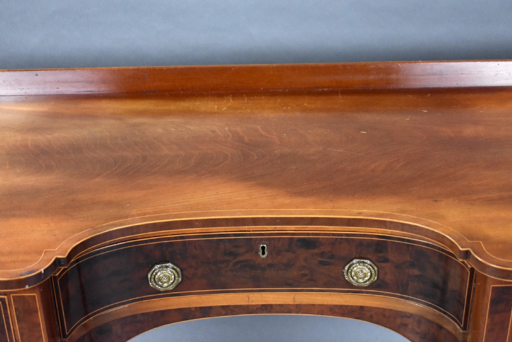 A nineteenth-century mahogany sideboard featuring a central kneehole arch, five inlaid drawers with brass rosette pull handles, and square tapered legs terminating in spade feet. View IX