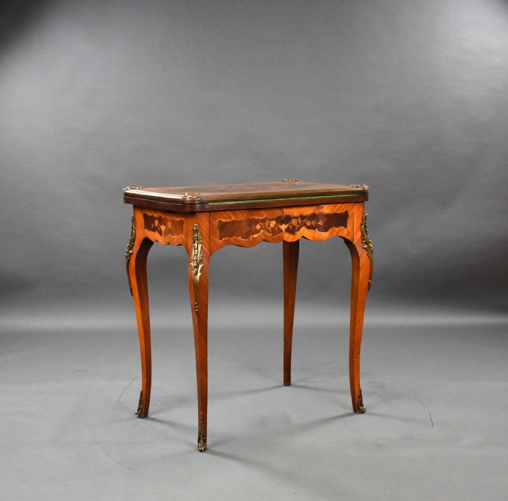 A Victorian French-style marquetry card table featuring slender cabriole legs with brass mounts and intricate floral inlay along the serpentine apron.