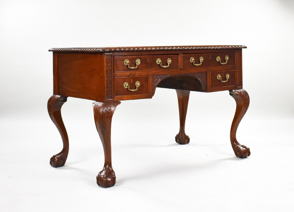 A dark brown mahogany Chippendale style writing table featuring cabriole legs with claw and ball feet, carved knees, gadrooned edging, and drawers with brass swan-neck handles.