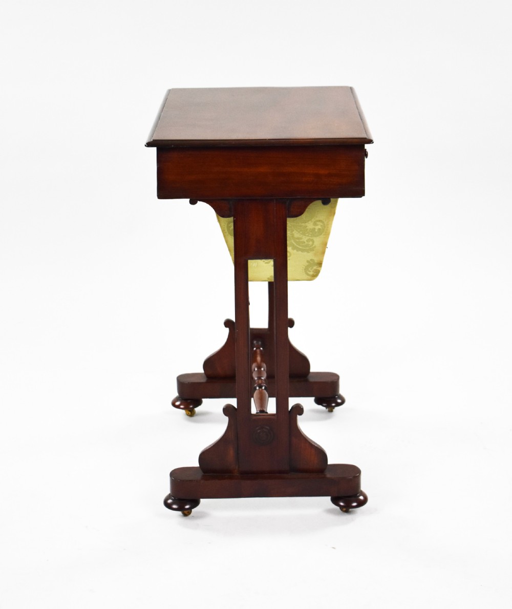 A Victorian mahogany work table featuring a single drawer with wooden knobs, a suspended yellow patterned fabric basket below, and a turned stretcher base set on castors. View VII