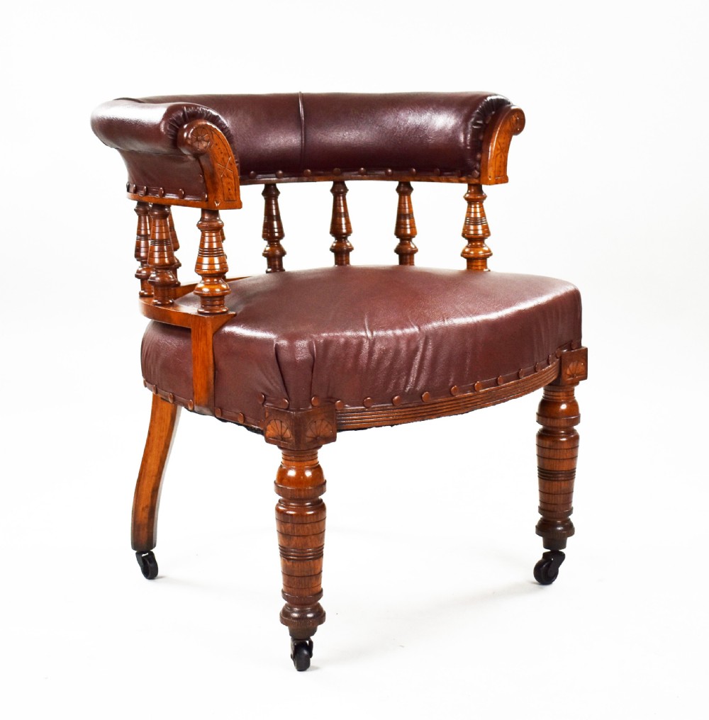 A Victorian oak tub armchair featuring brown leather upholstery, turned wooden spindles, stud detailing, and legs set on castors.