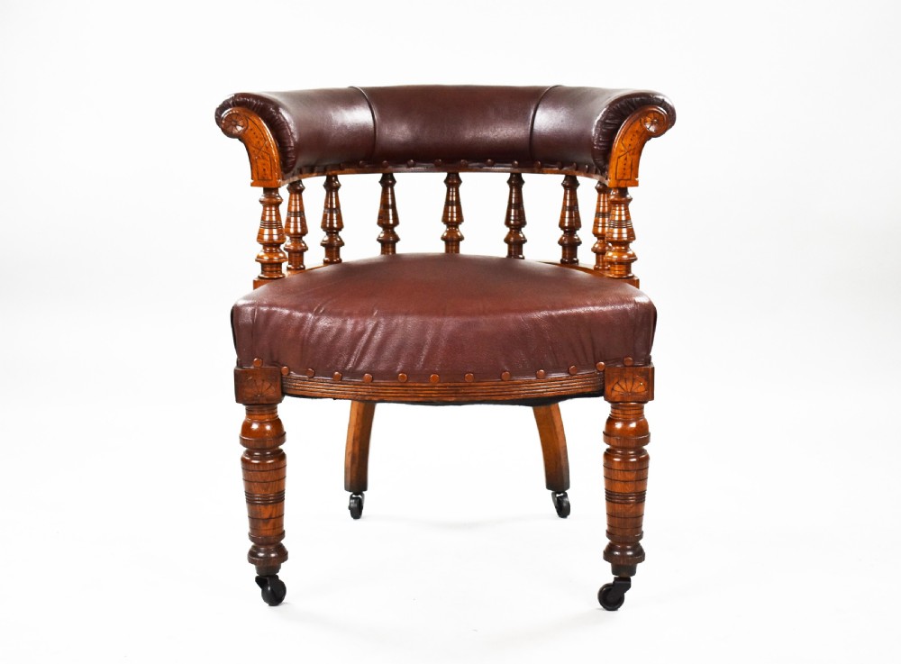 A Victorian oak tub armchair featuring brown leather upholstery, turned wooden spindles, stud detailing, and legs set on castors. View II