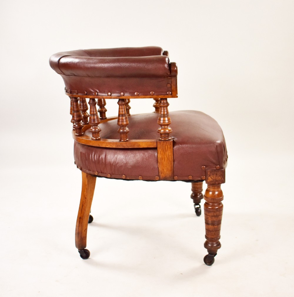 A Victorian oak tub armchair featuring brown leather upholstery, turned wooden spindles, stud detailing, and legs set on castors. View III