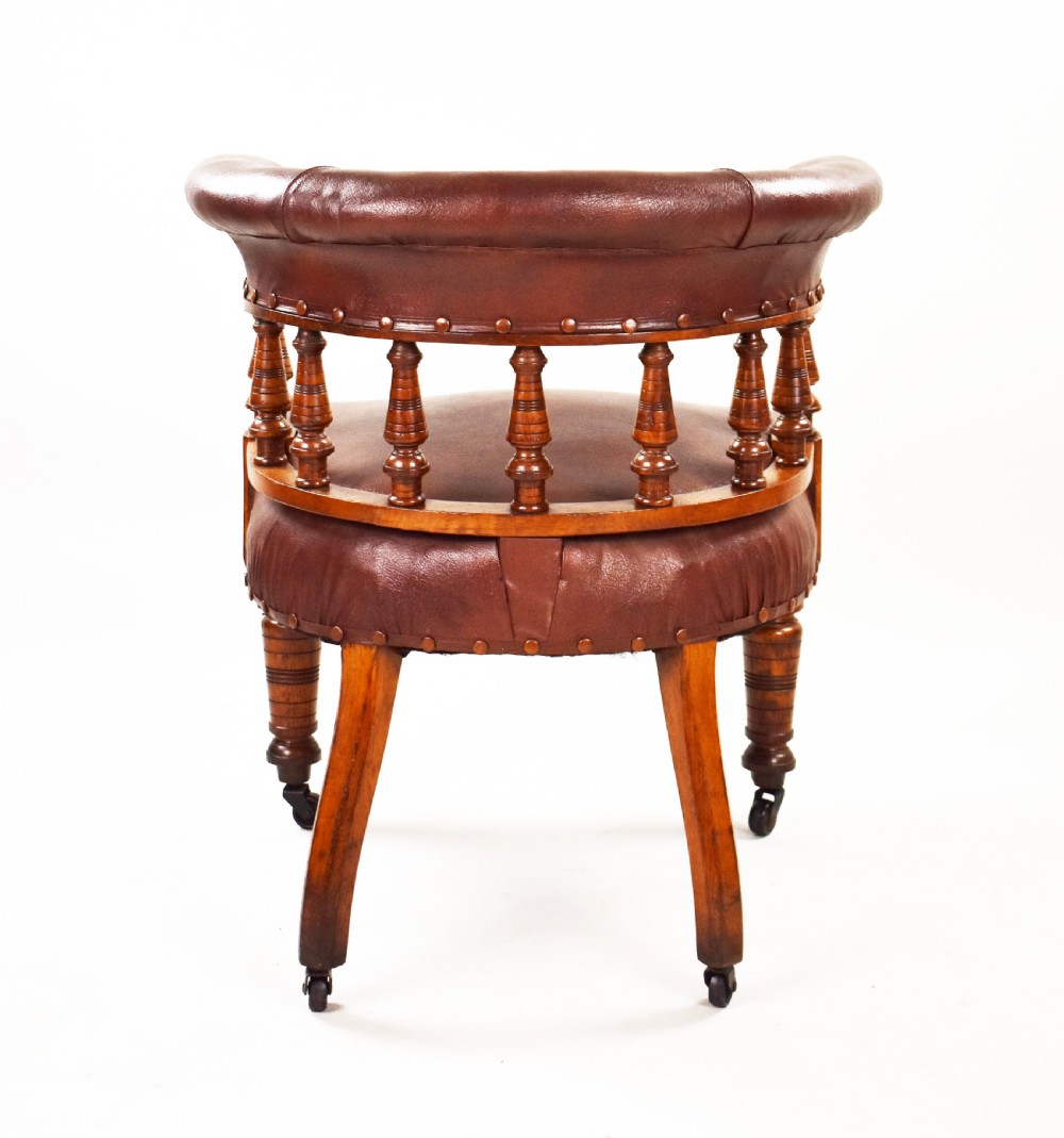 A Victorian oak tub armchair featuring brown leather upholstery, turned wooden spindles, stud detailing, and legs set on castors. View IV