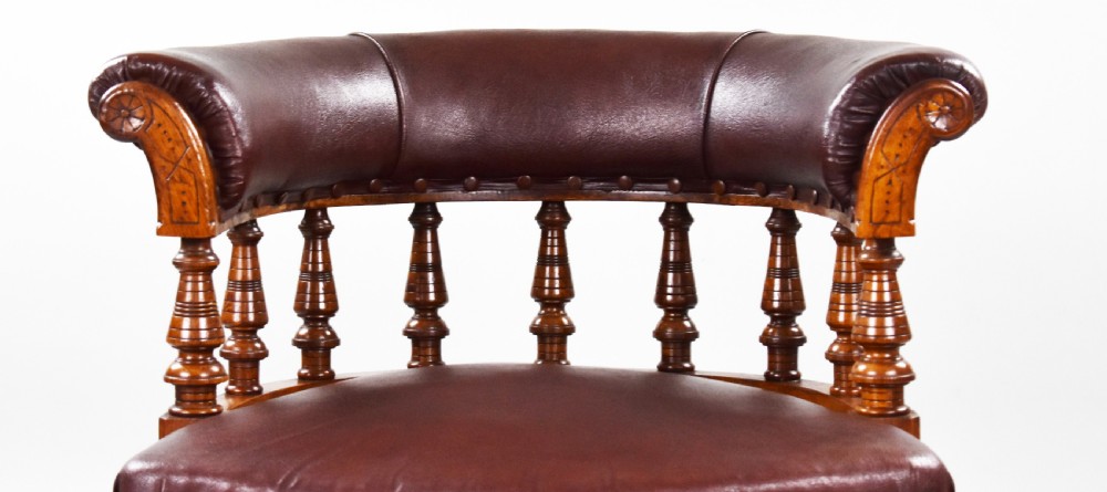 A Victorian oak tub armchair featuring brown leather upholstery, turned wooden spindles, stud detailing, and legs set on castors. View VI
