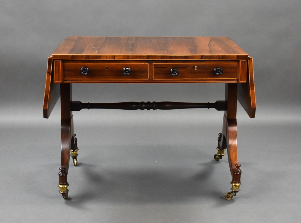 An early 19th-century Regency rosewood sofa table with drop leaves, boxwood stringing, two drawers, turned legs, and brass castors.