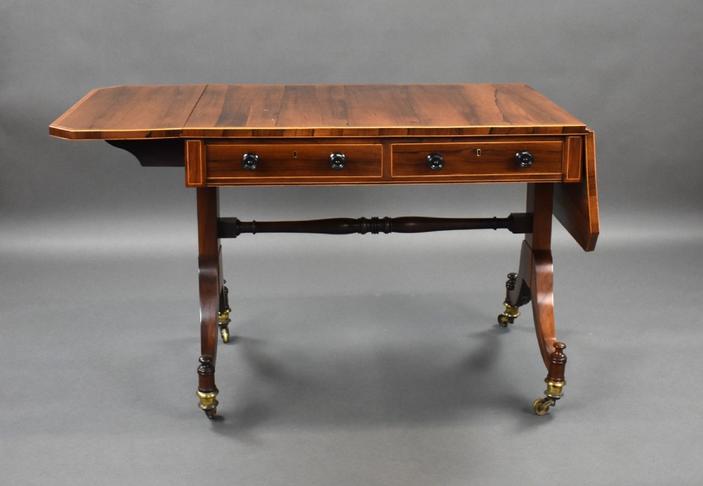 An early 19th-century Regency rosewood sofa table with drop leaves, boxwood stringing, two drawers, turned legs, and brass castors. View II