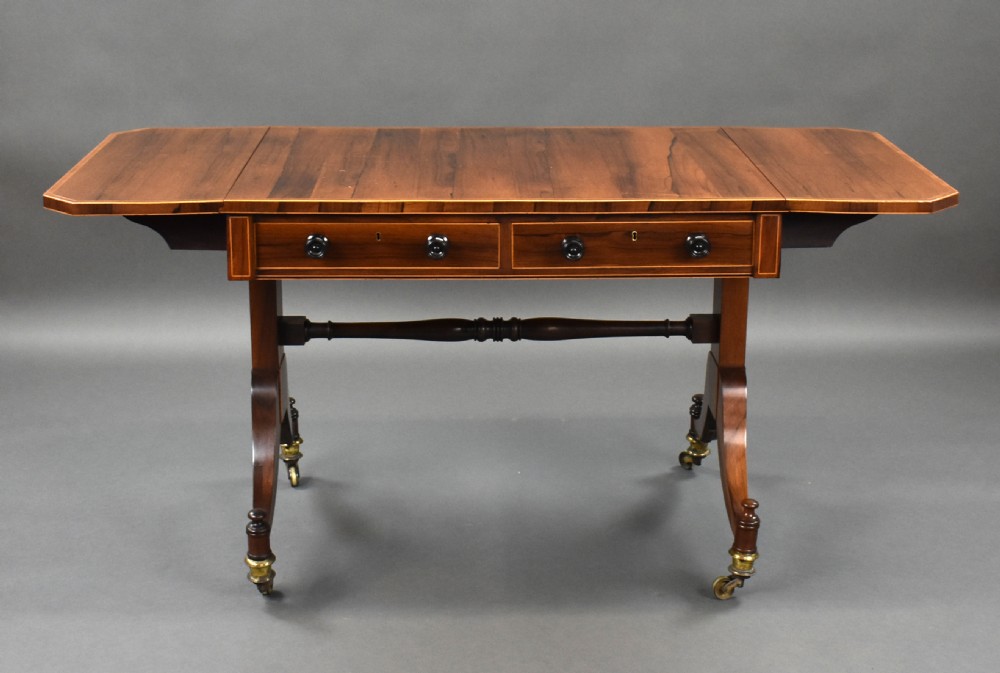 An early 19th-century Regency rosewood sofa table with drop leaves, boxwood stringing, two drawers, turned legs, and brass castors. View III
