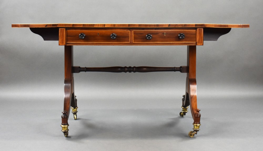 An early 19th-century Regency rosewood sofa table with drop leaves, boxwood stringing, two drawers, turned legs, and brass castors. View IV