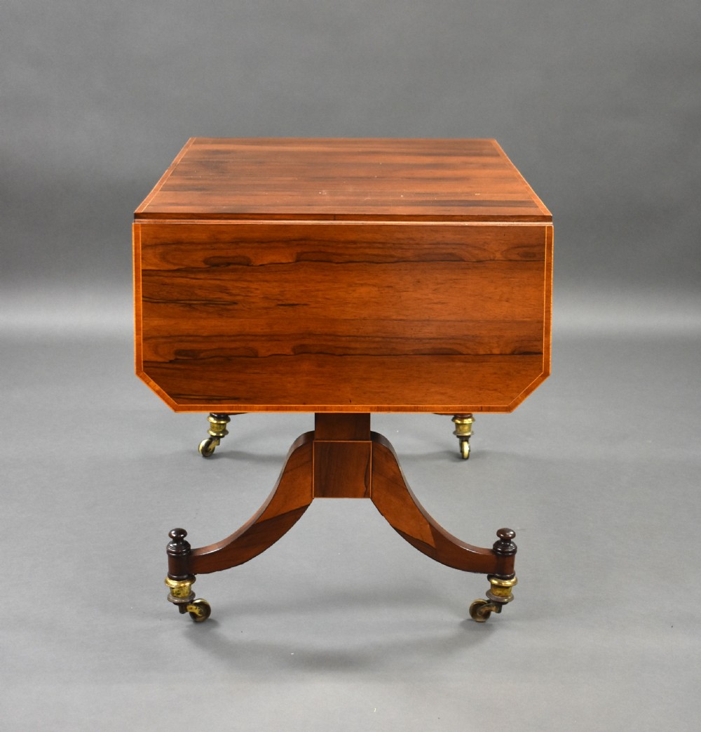 An early 19th-century Regency rosewood sofa table with drop leaves, boxwood stringing, two drawers, turned legs, and brass castors. View V