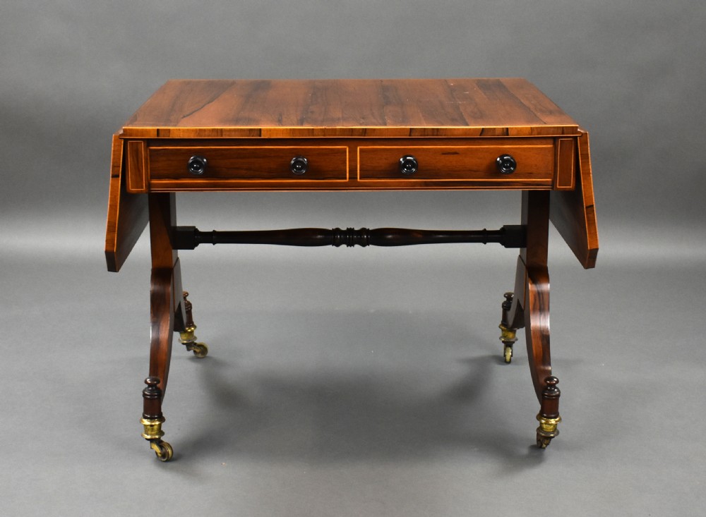 An early 19th-century Regency rosewood sofa table with drop leaves, boxwood stringing, two drawers, turned legs, and brass castors. View VI