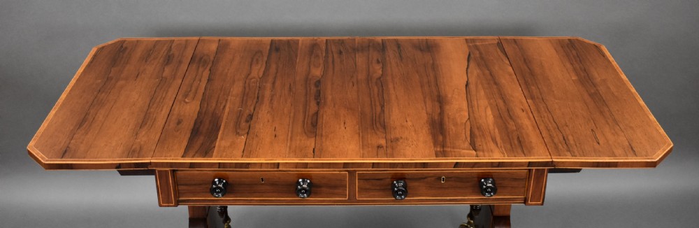 An early 19th-century Regency rosewood sofa table with drop leaves, boxwood stringing, two drawers, turned legs, and brass castors. View VIII