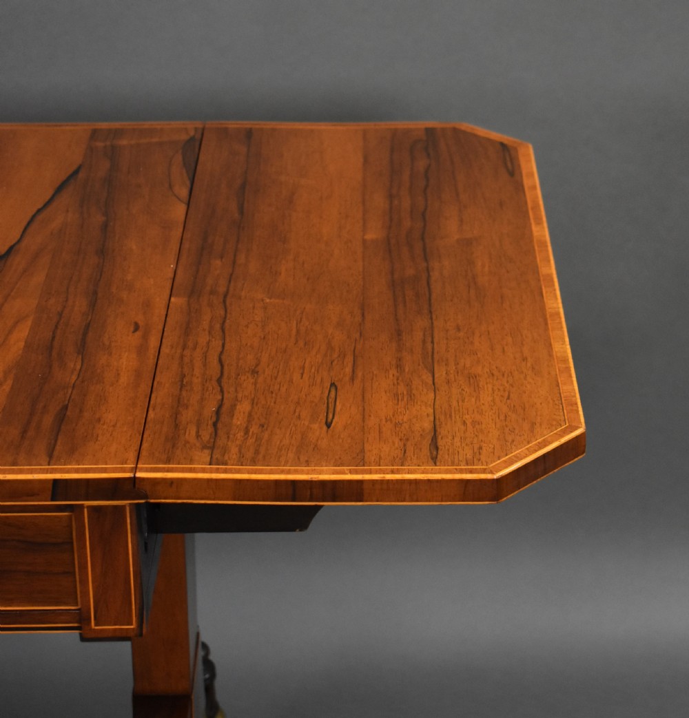 An early 19th-century Regency rosewood sofa table with drop leaves, boxwood stringing, two drawers, turned legs, and brass castors. View XI