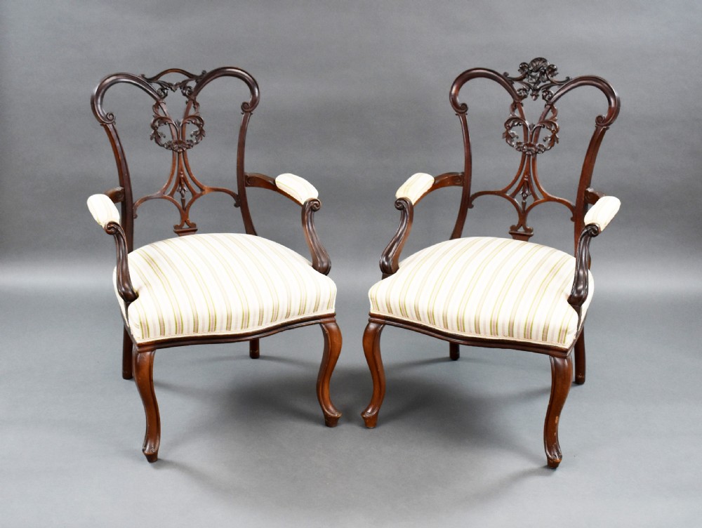 A pair of Victorian carved mahogany armchairs featuring pierced splat backs, padded armrests, and striped upholstery over cabriole legs.