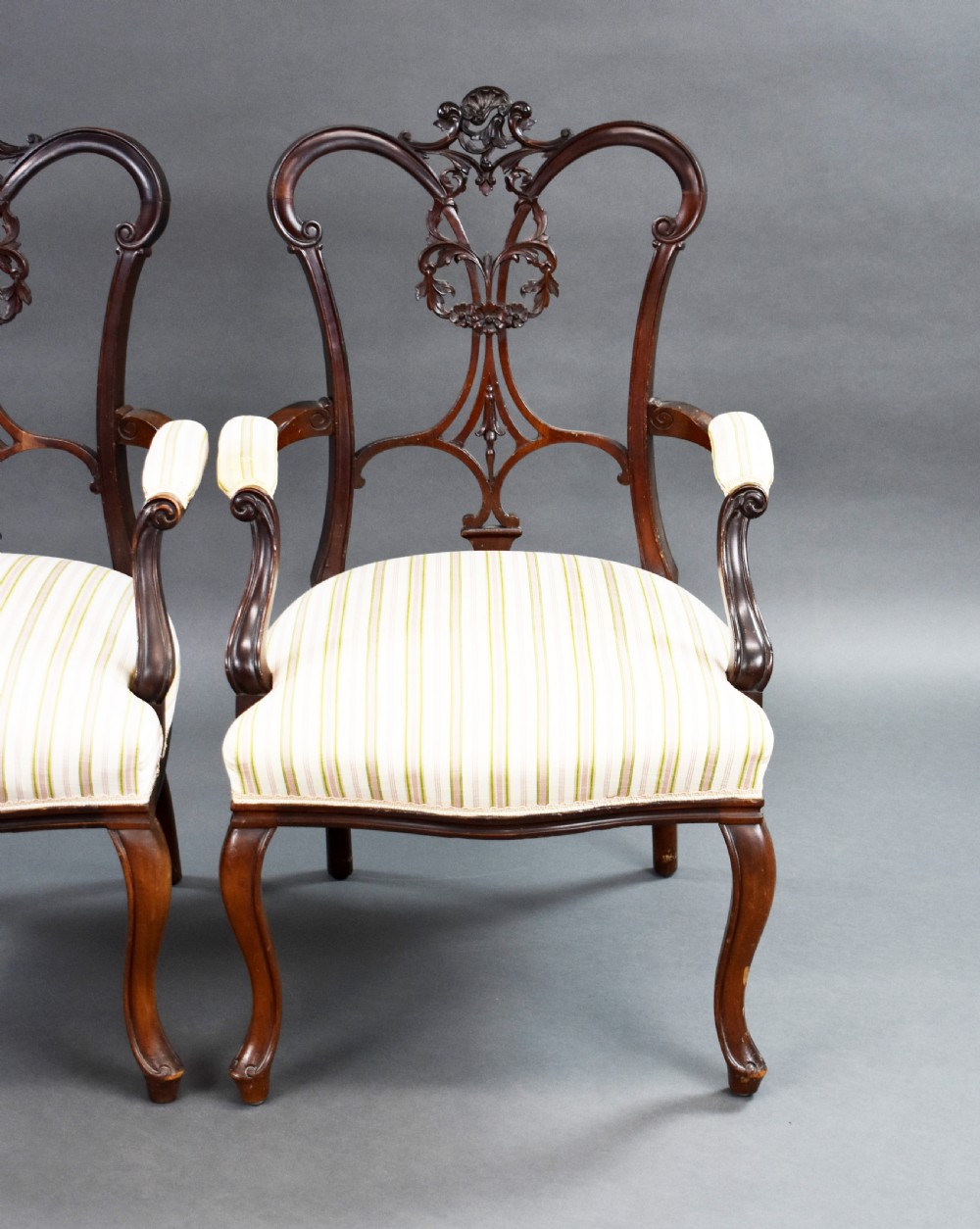 A pair of Victorian carved mahogany armchairs featuring pierced splat backs, padded armrests, and striped upholstery over cabriole legs. View IV