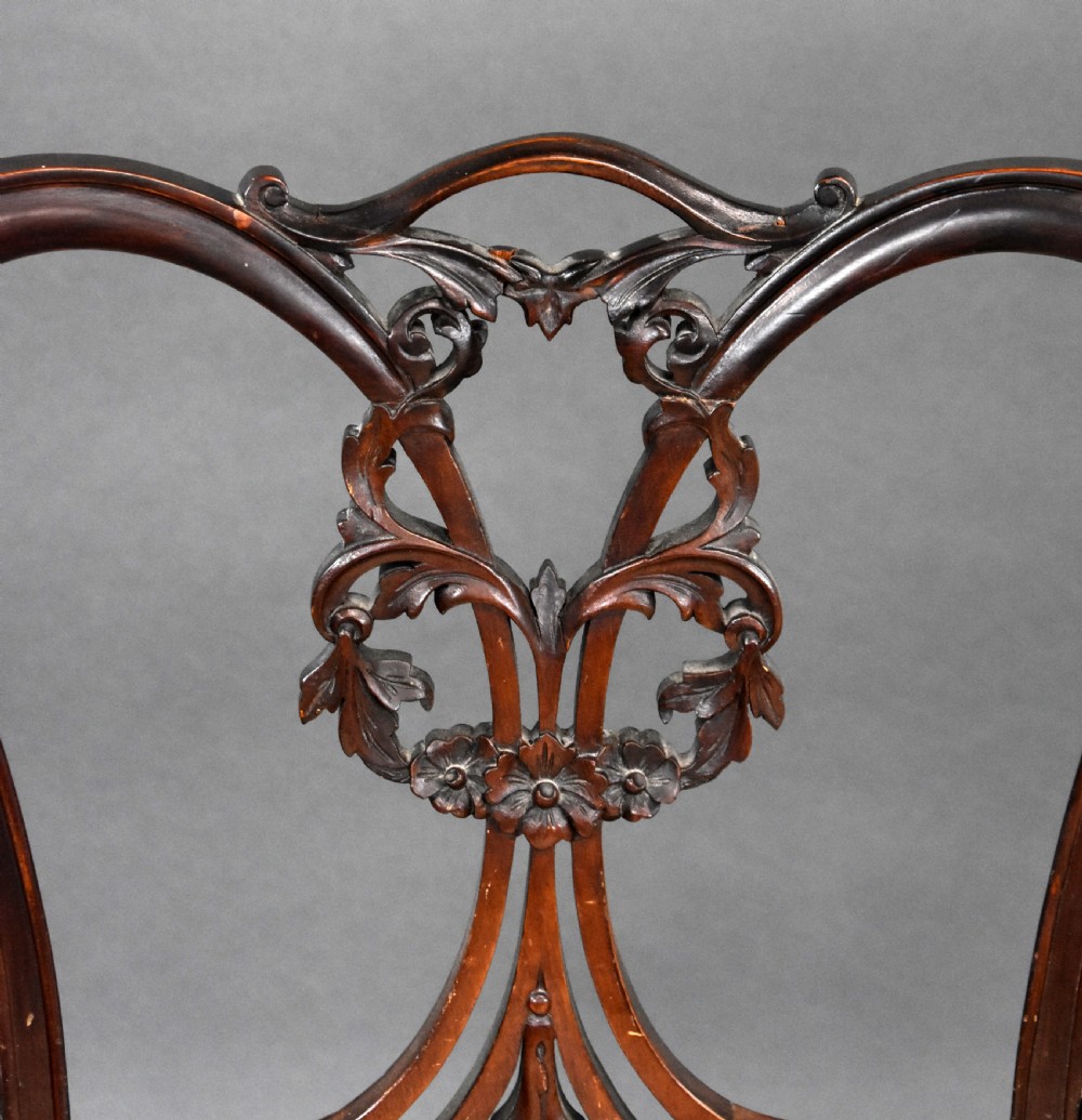 A pair of Victorian carved mahogany armchairs featuring pierced splat backs, padded armrests, and striped upholstery over cabriole legs. View VI