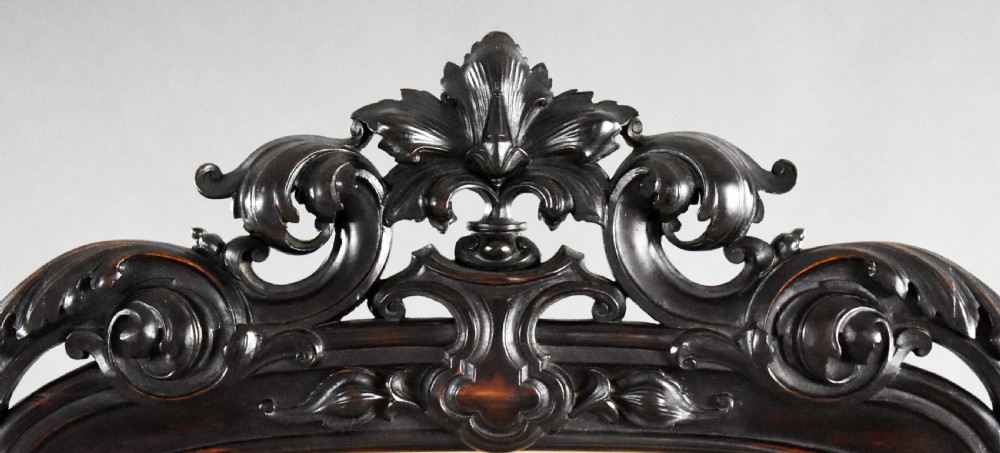 A dark carved wood Victorian fire screen framed around a central needlepoint panel depicting a parrot perched above two dogs. View IV