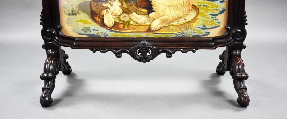 A dark carved wood Victorian fire screen framed around a central needlepoint panel depicting a parrot perched above two dogs. View VI